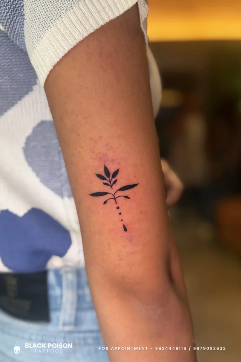 Tiny leaf sprig tattoo with solid black leaves and dotted stem on the upper arm at Black Poison Tattoo Studio, Ahmedabad