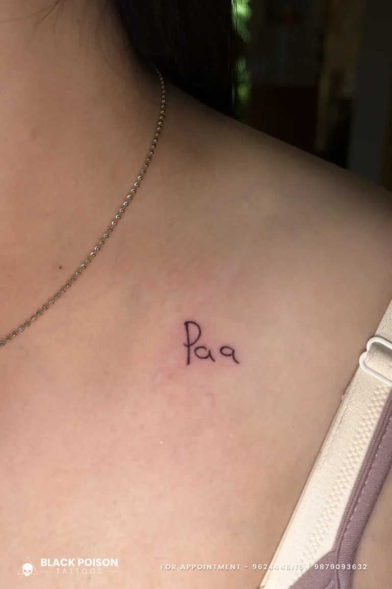 Tiny handwriting-style Paa tattoo in black ink just below the collarbone at Black Poison Tattoo Studio, Ahmedabad