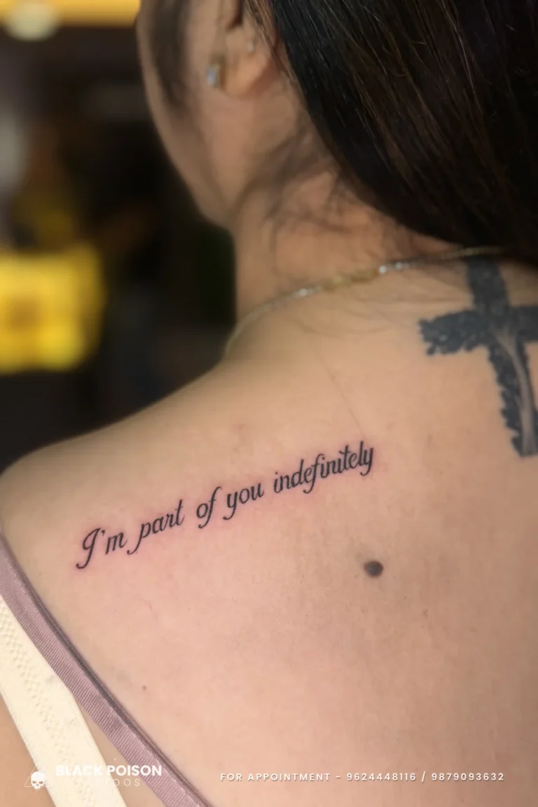 Cursive I'm part of you indefinitely tattoo on the upper back below a black cross at Black Poison Tattoo Studio, Ahmedabad