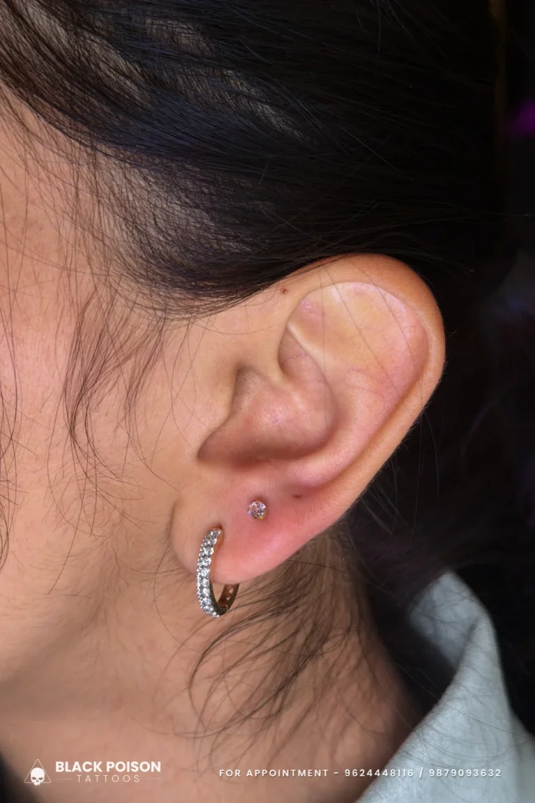 Fresh second lobe piercing with a pink stone stud above a crystal-set huggie hoop at Black Poison Tattoo Studio, Ahmedabad