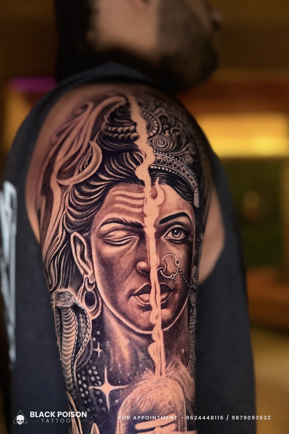 Close-up of a black and grey Ardhanarishvara tattoo, half Shiva and half Parvati, split by a trishul line on the upper arm