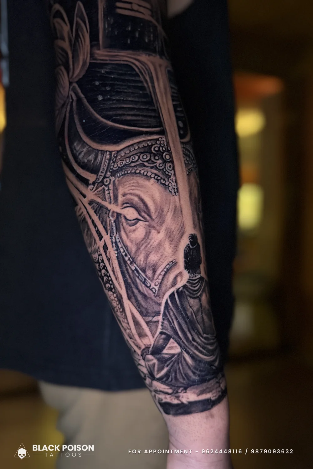 Black and grey forearm tattoo of Nandi the bull in an ornate headdress beside a Shivling and a small seated devotee