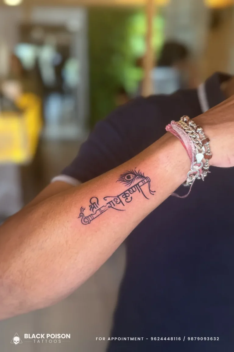 Radhe Krishna Devanagari tattoo with flute and peacock feather on the forearm at Black Poison Tattoo Studio, Ahmedabad