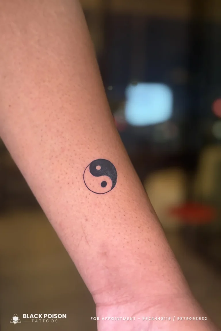 Small solid black yin yang symbol tattooed on the outer wrist and lower forearm at Black Poison Tattoo Studio, Ahmedabad
