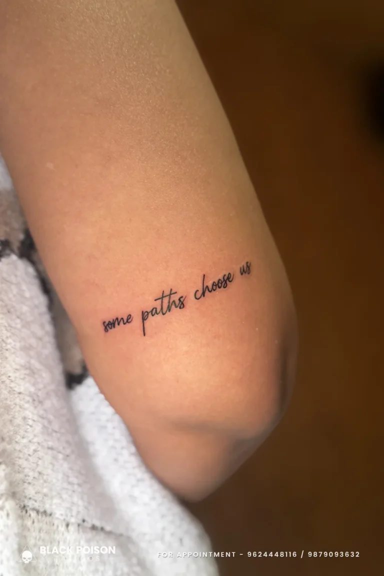 Hairline cursive tattoo reading some paths choose us on the back of the arm at Black Poison Tattoo Studio, Ahmedabad