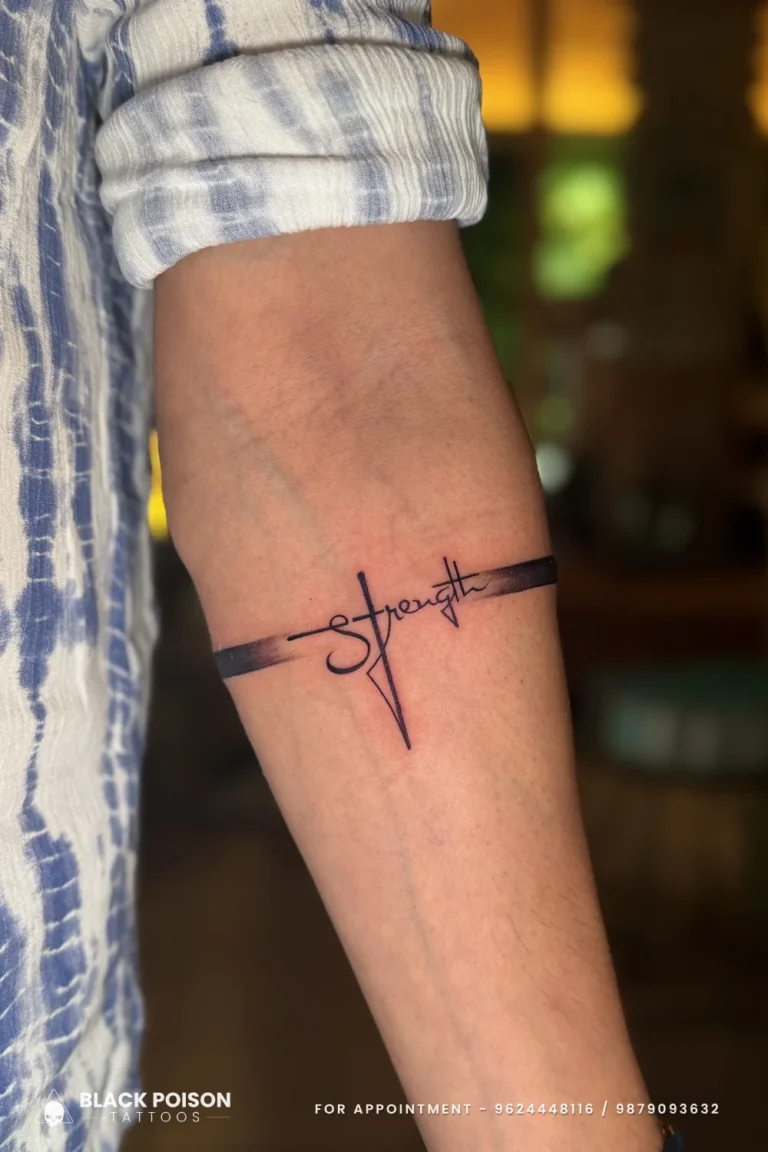 Cursive Strength tattoo with a cross for the t and a thin armband on the forearm at Black Poison Tattoo Studio, Ahmedabad