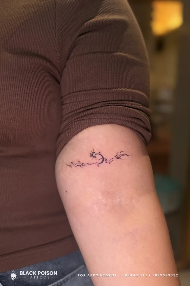 Fine line black sun, crescent moon and cloud band tattoo on the inner upper arm at Black Poison Tattoo Studio, Ahmedabad