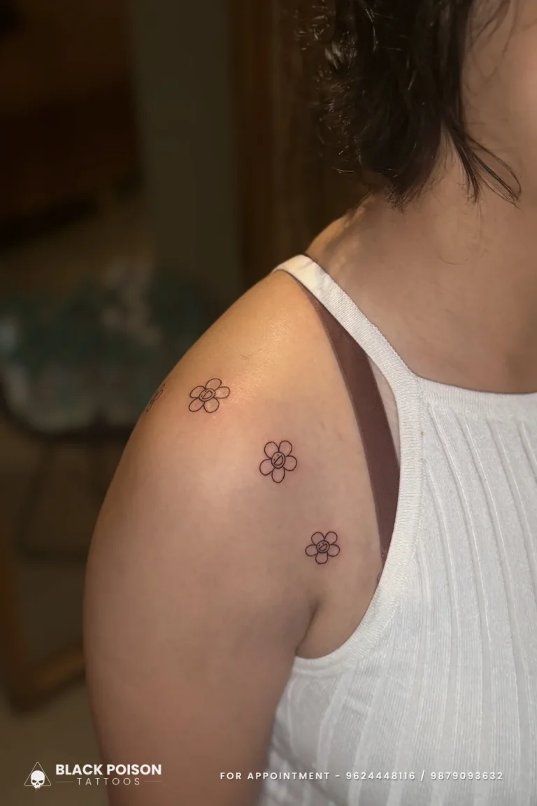 Three tiny fine line daisy outlines in a loose diagonal on the back of the shoulder at Black Poison Tattoo Studio, Ahmedabad