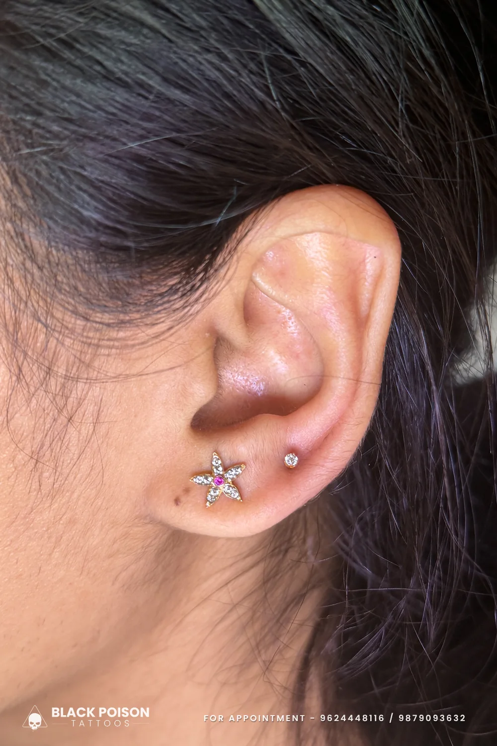 Tragus piercing with a jewelled star-shaped flower stud set with a pink centre stone and a tiny crystal stud on the lobe