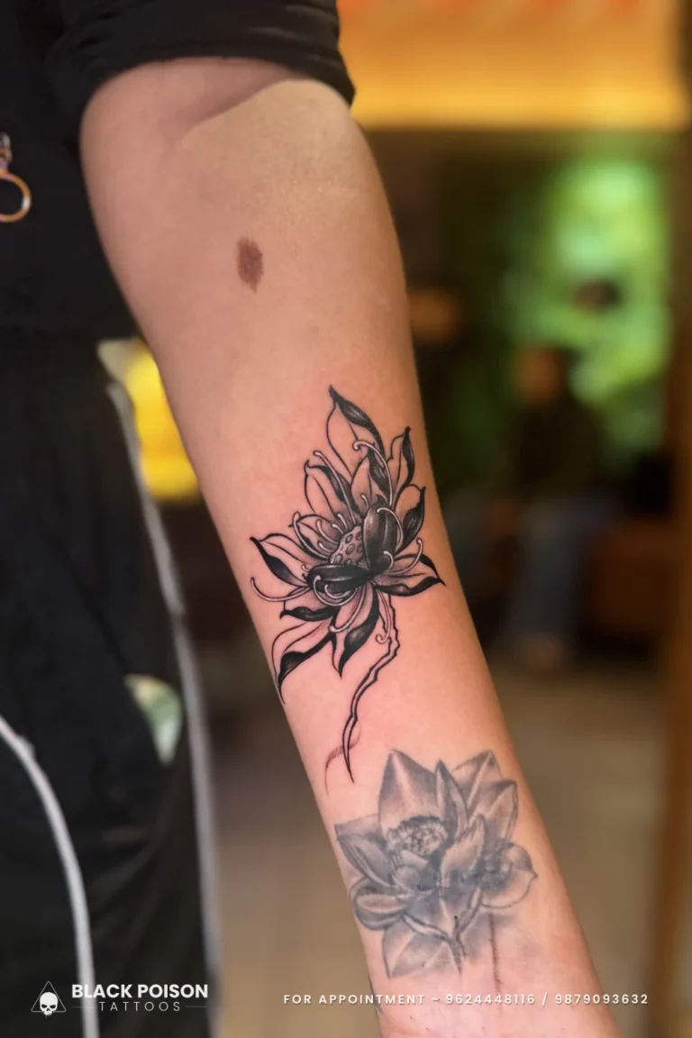 Black and grey tattoo of two lotus flowers on one stem down the inner forearm at Black Poison Tattoo Studio, Ahmedabad