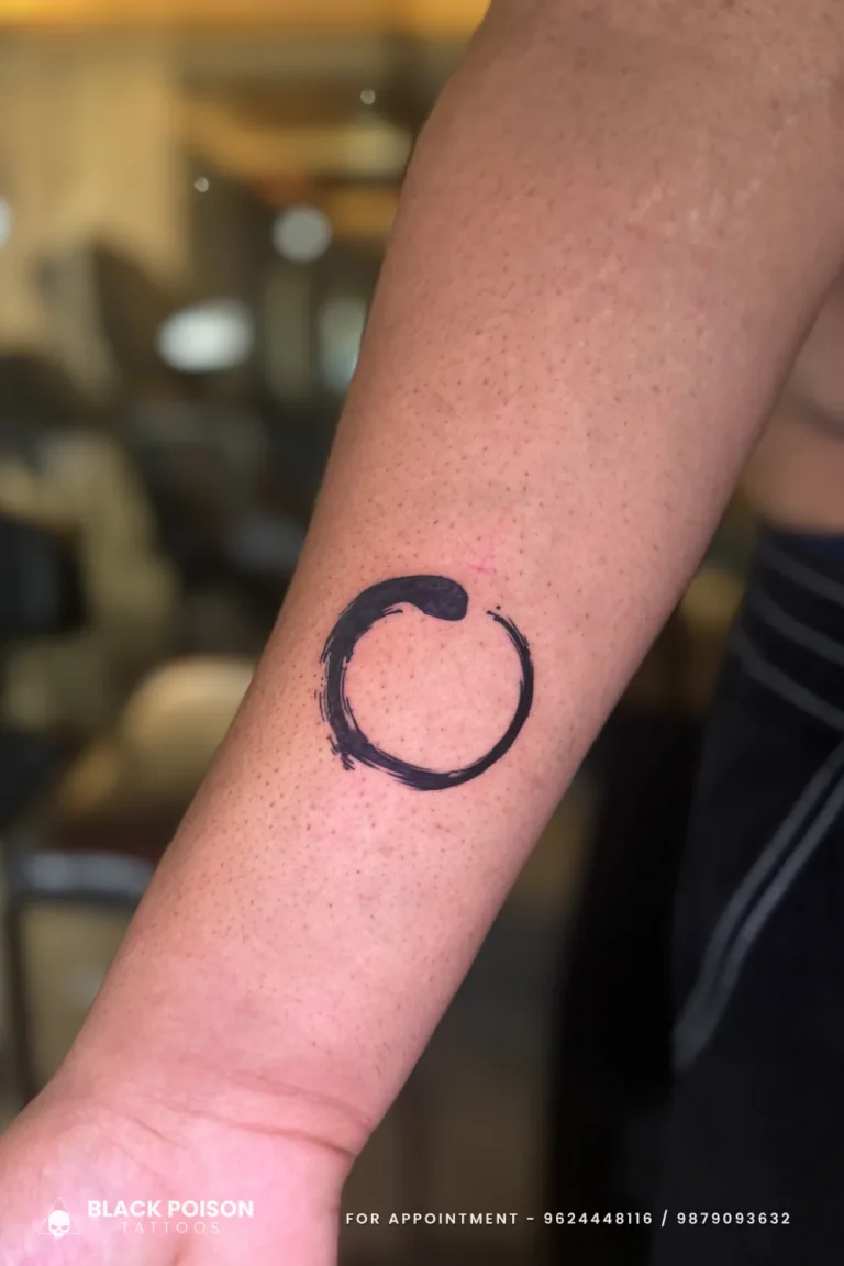 Bold black enso circle brushstroke tattoo with an open gap on the outer forearm at Black Poison Tattoo Studio, Ahmedabad